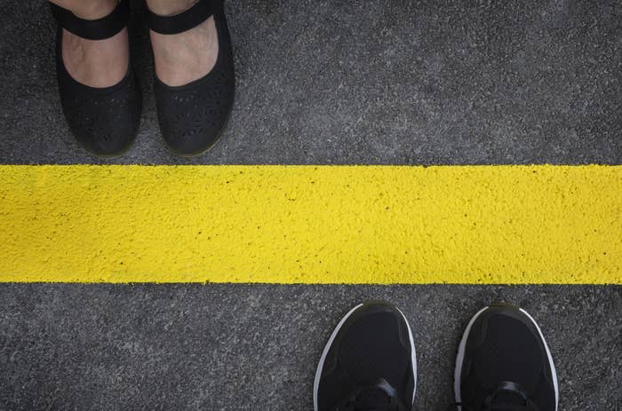 Legs of a couple standing opposite each other divided by the yellow asphalt line top view