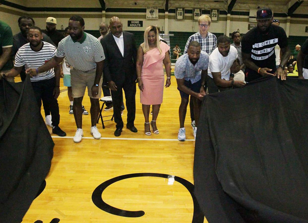 Dru Joyce II, center, boys basketball coach at St. Vincent-St. Mary High School, and his wife, Carolyn — surrounded by his former players, Sian Cotton, left, his son Cameron Joyce, Athletic Director Willie McGee, his son Dru Joyce III, Corey Jones, Brandon Weems and LeBron James — unveil the new Coach Dru Joyce Court during a dedication ceremony Sunday at the school's LeBron James Arena in Akron.