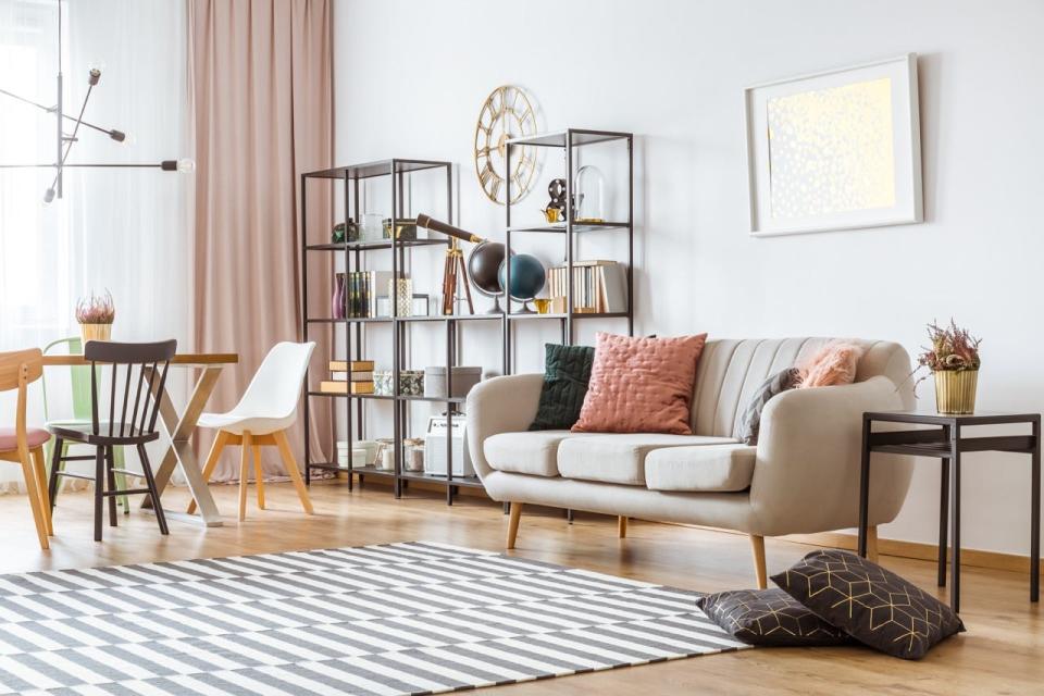 Curved beige couch next to metal shelving unit in front of checkered rug