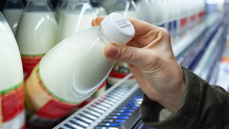 A hand grabbing a bottle of milk at a store