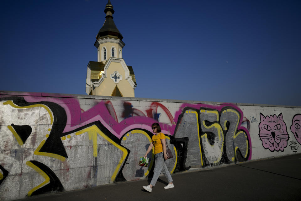 A woman walks in front of graffiti on a wall in Kyiv, Ukraine, Friday, June 10, 2022. With war raging on fronts to the east and south, the summer of 2022 is proving bitter for the Ukrainian capital, Kyiv. The sun shines but sadness and grim determination reign. (AP Photo/Natacha Pisarenko)