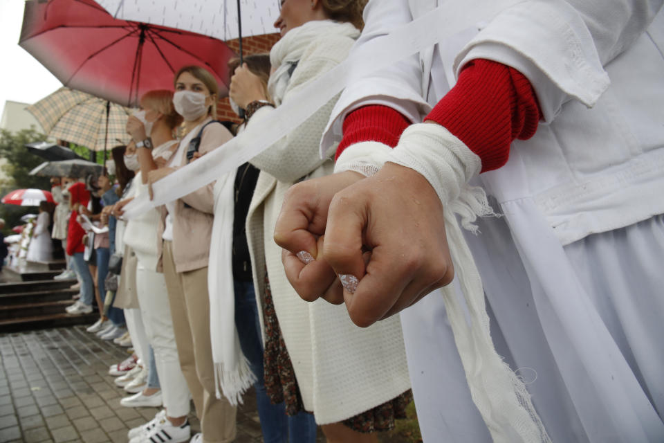 A woman wrapped her arms with ribbon, a symbol of protest, as protesters stand in front of the Church of Saints Simon and Helena during a rally in Minsk, Belarus, Thursday, Aug. 27, 2020. Russian President Vladimir Putin warned that he stands ready to send police to Belarus if protests there turn violent, but added in an interview broadcast Thursday that there is no such need now and voiced hope for stabilizing the situation in the neighboring country. (AP Photo/Dmitri Lovetsky)