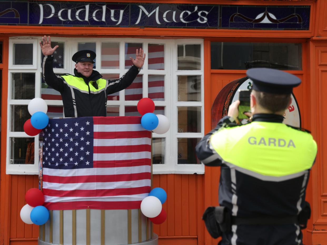 An Irish police officer poses for a colleague to take a photo as last minute preparation are made with bunting and US flags put up in Ballina (AP)