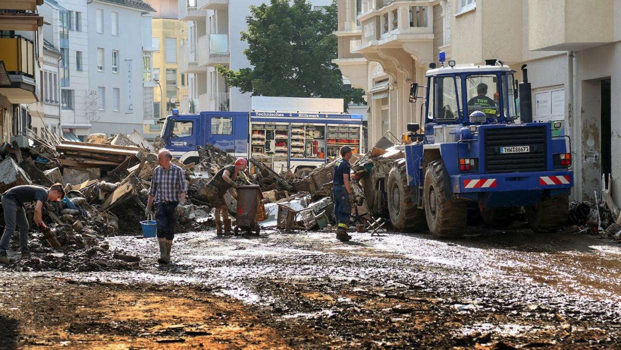 Mitarbeiter des Technischen Hilfswerks (THW) helfen bei Aufräumarbeiten nach der Unwetterkatastrophe in einer verschlammten Straße.