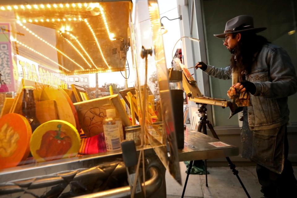 Artist Francisco Palomares works on a painting next to his converted fruit cart in the Arts District in Los Angeles.