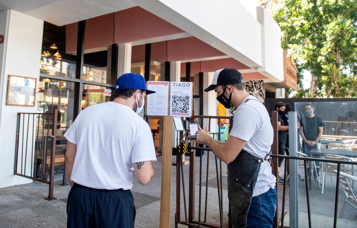 A server shows a client how to access the menu and place his order using his smartphone at Tiago Cafe amid the coronavirus pandemic on August 7, 2020, in Hollywood, Ca.