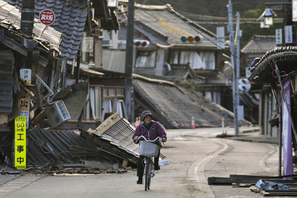 A woman bikes amid damaged houses in Noto town in the Noto peninsula facing the Sea of Japan, northwest of Tokyo, Tuesday, Jan. 2, 2024, following Monday's deadly earthquake. (AP Photo/Hiro Komae)