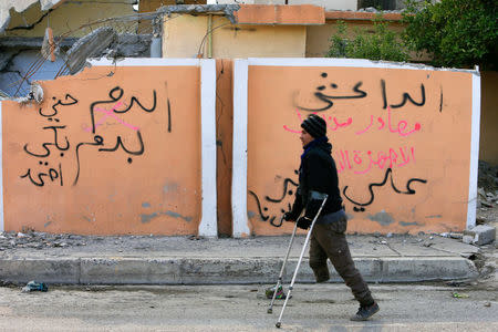 A handicapped man walks past text on a wall reading that the house belongs to Islamic State militants in Qayyara, Iraq, December 6, 2016. Picture taken December 6, 2016. REUTERS/Alaa Al-Marjani