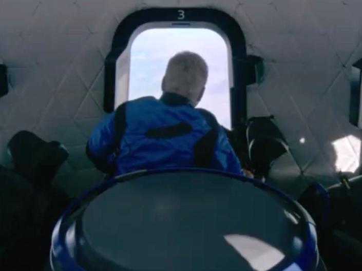 william shatner in a blue flight suit staring out spaceship window