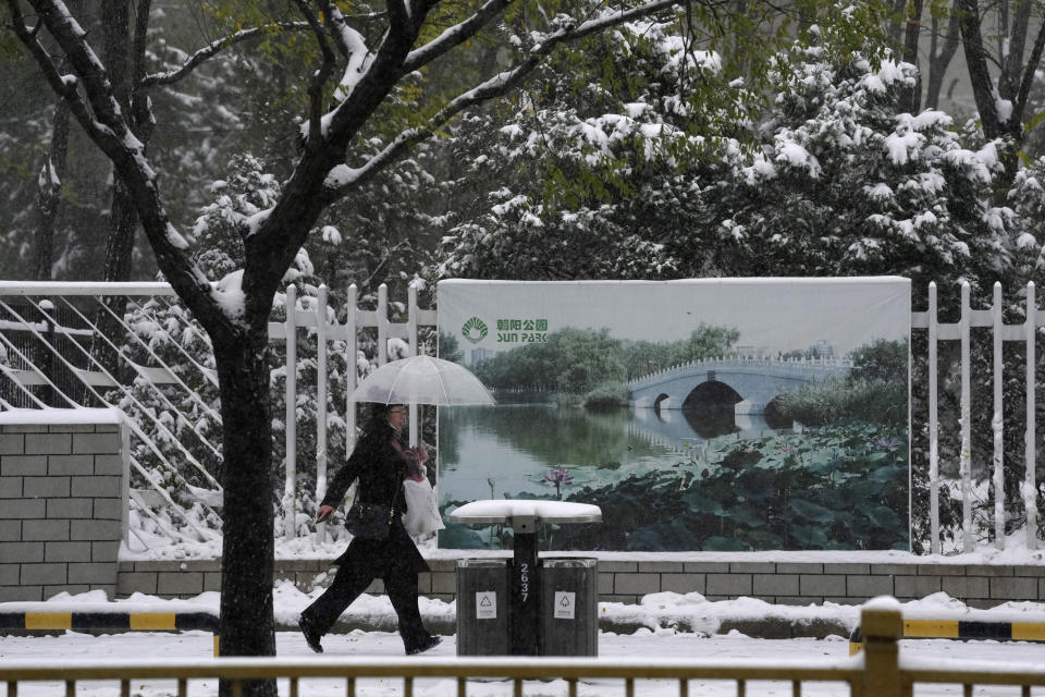 A resident walks past a park billboard showing summer time as it snows in Beijing, China, Sunday, Nov. 7, 2021. An early-season snowstorm has blanketed much of northern China including the capital Beijing, prompting road closures and flight cancellations. (AP Photo/Ng Han Guan)