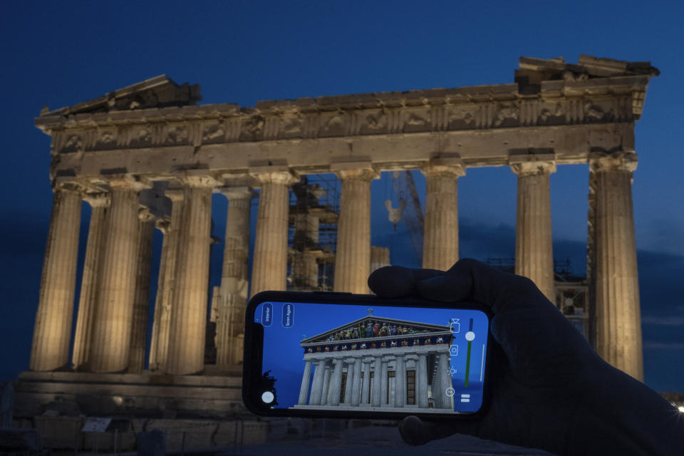 A woman holds up a mobile phone showing a digitally overlayed virtual reconstruction of the ancient Parthenon temple, at the Acropolis Hill in Athens, Greece on Tuesday, June 13, 2023. Greece has become a late but enthusiastic convert to new technology as a way of displaying its famous archaeological monuments and deepening visitors' knowledge of ancient history. The latest virtual tour on offer is provided by a mobile app that uses Augmented Reality to produce digital overlays that show visitors at the Acropolis how the site and its sculptures looked 2,500 ago. (AP Photo/Petros Giannakouris)