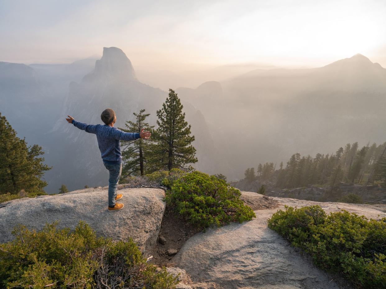 Young man standing arms outstretched on top of Yosemite valley, USA at sunrise