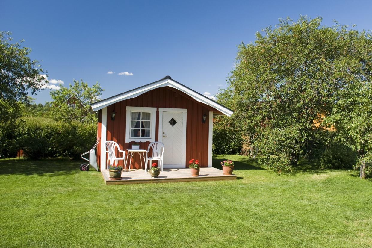 red tiny house with porch in an idyllic area with cherry trees in the background