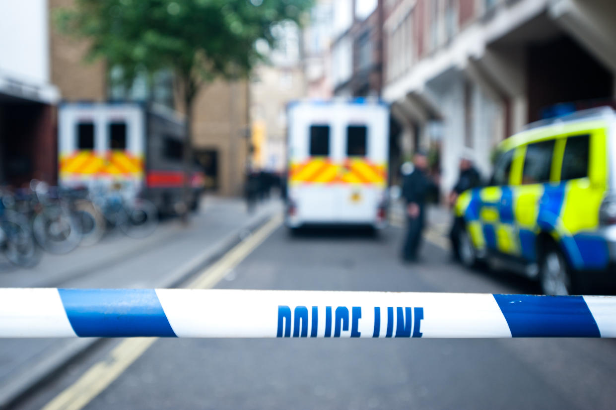 Police officers and vans behind safety police line tape.