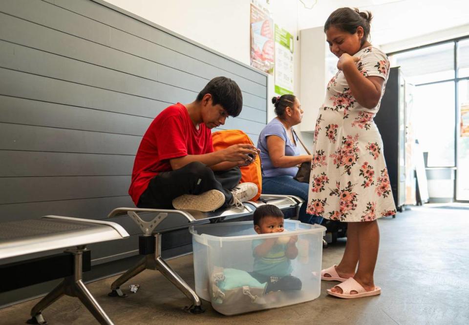 Angel de la Cruz, left, plays a game on his phone while his brother Ian de la Cruz drinks milk and their mother, Catalina Luis stands near by on Community Laundry Day at Leah’s Laundromat.