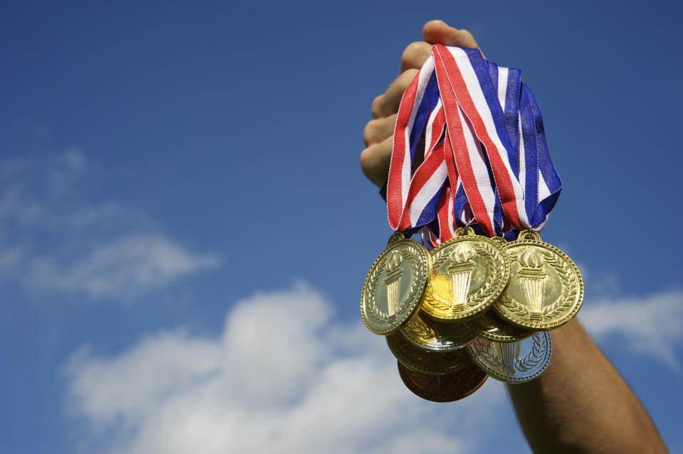 Hand holds up a bunch of gold, silver, and bronze medals in bright blue sky