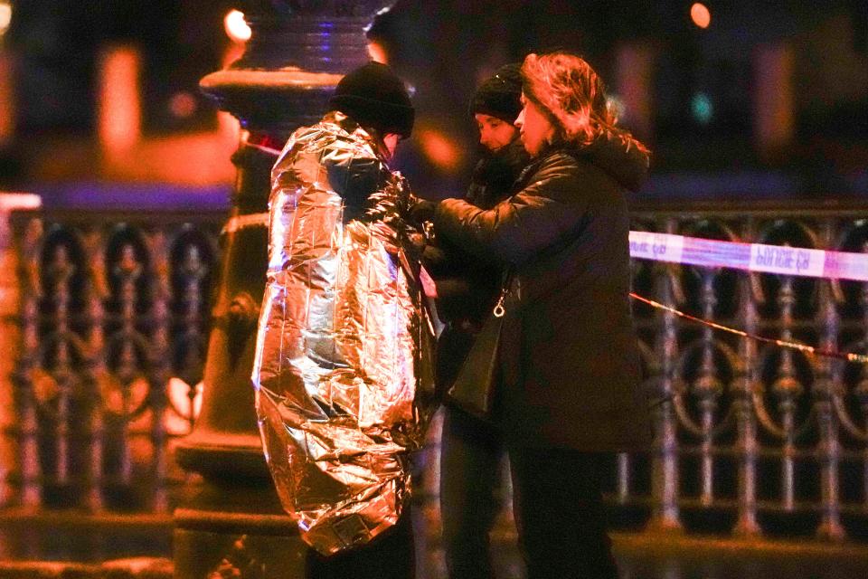 Women attend to a person wrapped in a thermal blanket near the building of Philosophical Faculty of Charles University in downtown Prague, Czech Republic, Thursday, Dec. 21, 2023. A mass shooting in downtown Prague killed several people and injured others, and the person who opened fire also is dead, Czech police and the city's rescue service said Thursday.