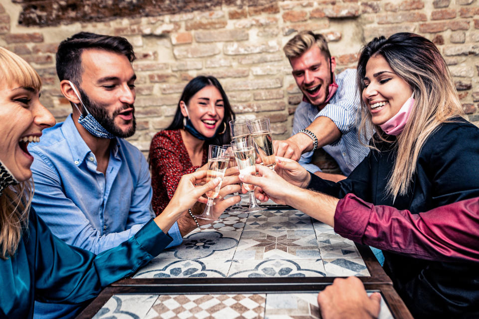 Christmas party! Young people with face mask toasting with champagne flutes in coronavirus time - Multiethnic friends congratulating each other on the new year eve - Celebration and nightlife, holiday background, selective focus