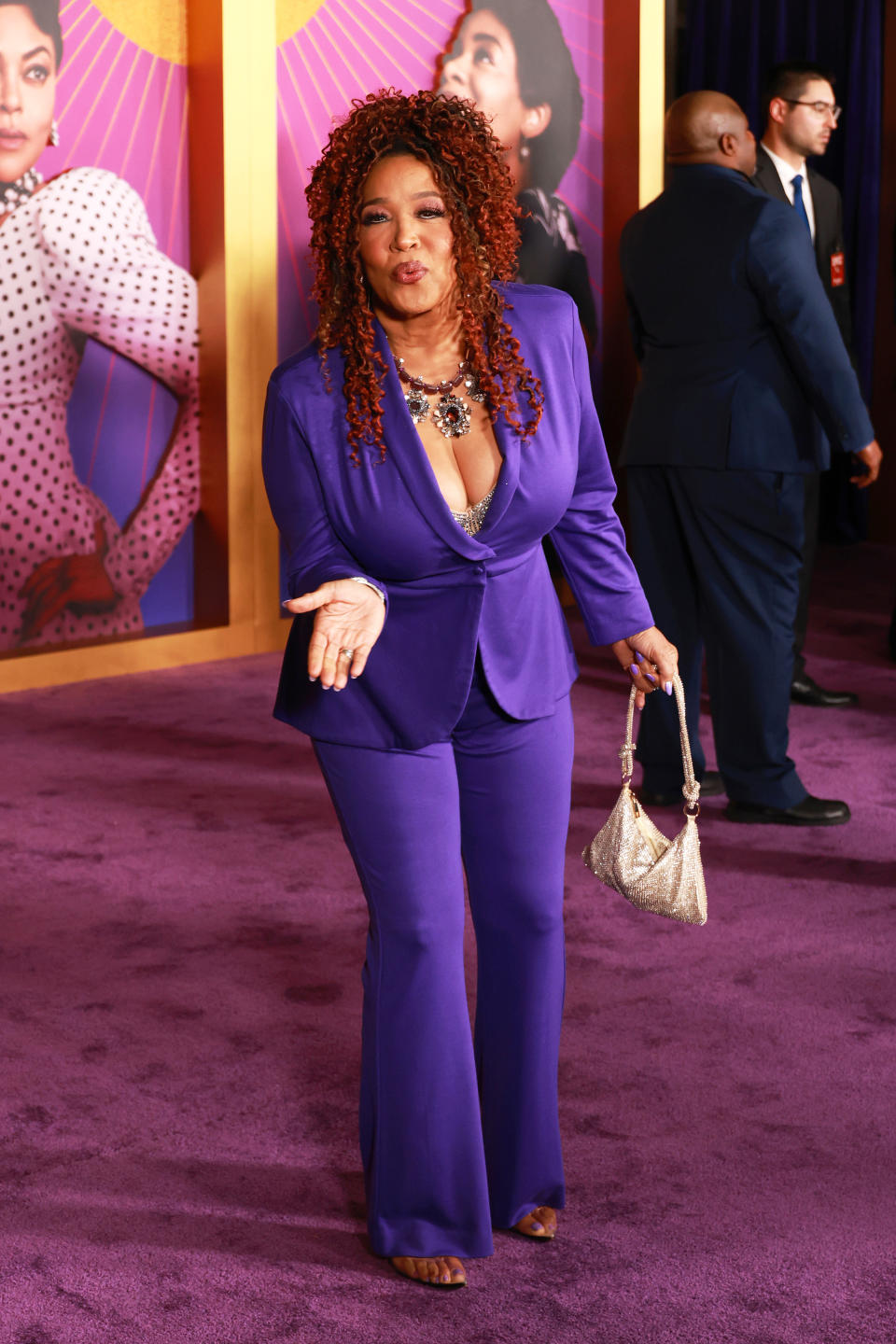 Kym in a purple pantsuit blowing a kiss