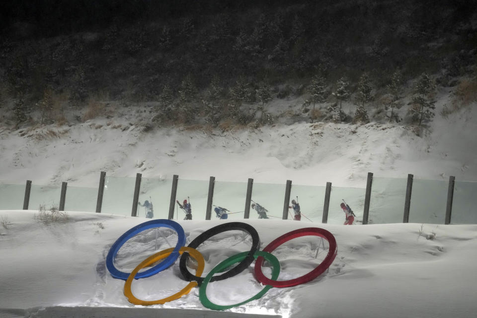 Biathletes ski uphill near the Olympics rings during the men's 12.5-kilometer pursuit race at the 2022 Winter Olympics, Sunday, Feb. 13, 2022, in Zhangjiakou, China. (AP Photo/Kirsty Wigglesworth)