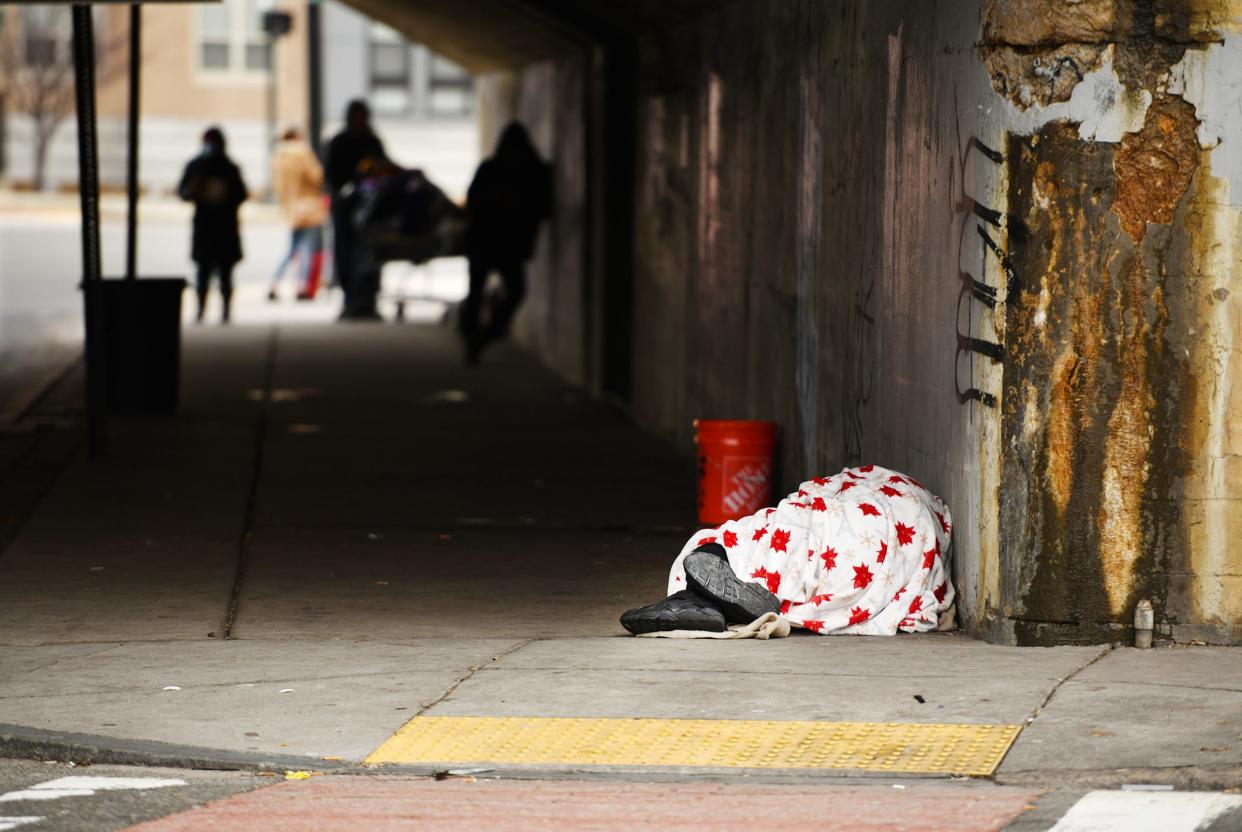 A man sleeps with only his shoes sticking out, under the Green Street bridge in Worcester as other people panhandle at the other end.