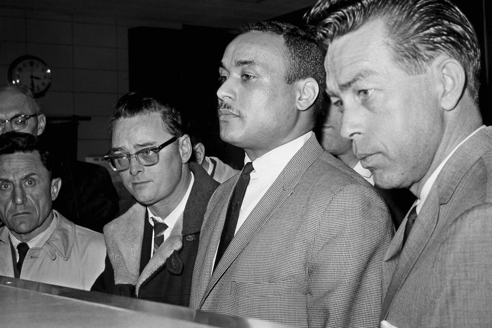 FILE — Khalil Islam, center, is booked as the third suspect in the slaying of Malcolm X, in New York, March 3, 1965. Islam, previously known as Thomas 15X Johnson, one of two men convicted in the assassination of Malcolm X, is set to be cleared after more than half a century, with prosecutors now saying authorities withheld evidence in the civil rights leader's killing, according to a news report Wednesday, Nov. 17, 2021. Detective John Keeley is at right. (AP Photo, File)