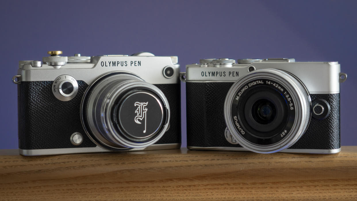  The Olympus PEN-F sat next to an Olympus PEN E-P7, on a wooden surface against a blue background. 