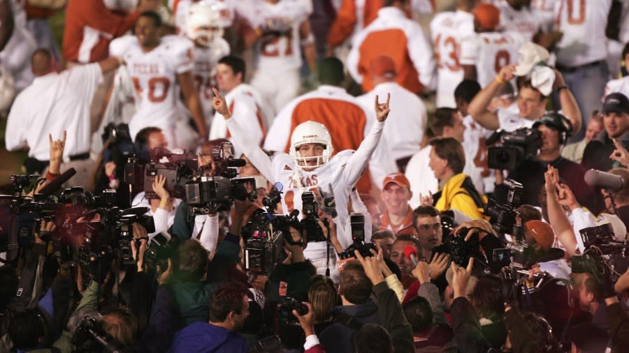 Dozens of cameras surround Dusty Mangum while he is being carried off the field, showing the Texas "Hook 'em" sign with both hands.