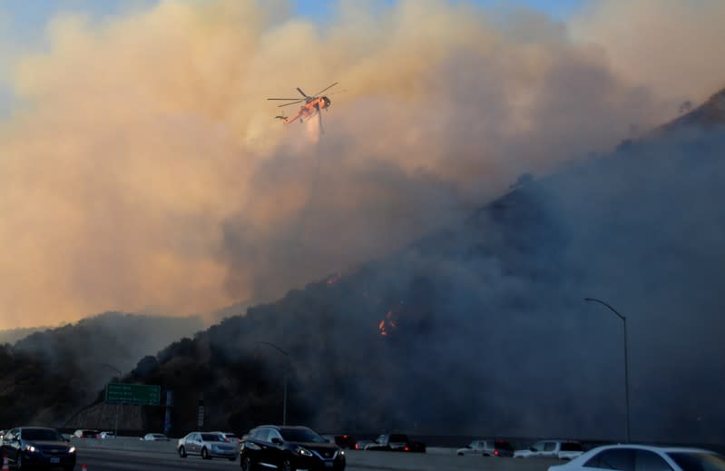 A firefighting helicopter drops water on the Getty Fire as it burns next to the 405 Freeway in the hills of West Los Angeles