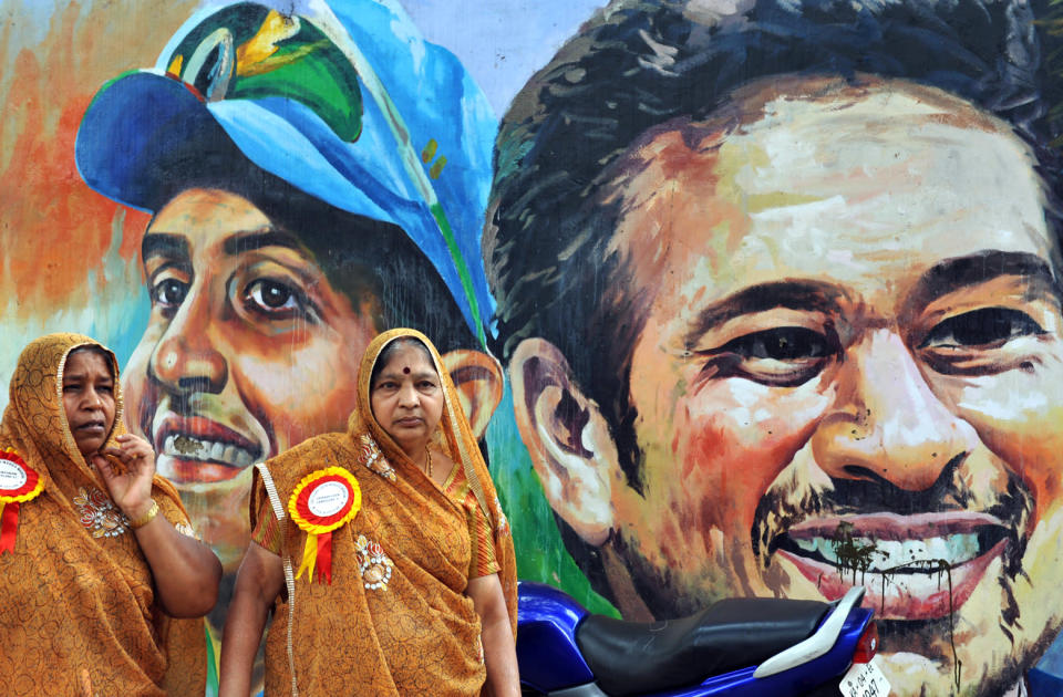 Sari-clad women stand infront of a mural depicting former Indian cricket captain Sourav Ganguly and cricketer Sachin Tendulkar in Bangalore.<br>AFP PHOTO/Dibyangshu SARKAR