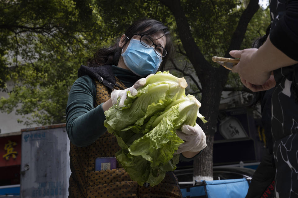 In this Monday, April 6, 2020, photo, a resident volunteer hands over vegetables to a resident outside a community in Wuhan in central China's Hubei province. Some farmers are finding temporary outlets for sales through volunteers in Wuhan helping the elderly and other vulnerable people get food supplies. They buy direct from farmers and arrange delivery to apartment complexes. (AP Photo/Ng Han Guan)