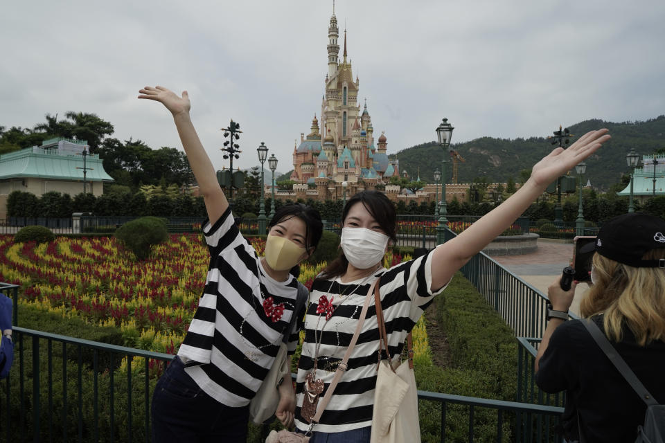 Visitors wearing face masks pose for photos at the Hong Kong Disneyland, Friday, Sept. 25, 2020. Hong Kong Disneyland reopened its doors to visitors after closed temporarily due to the coronavirus outbreak. (AP Photo/Kin Cheung)