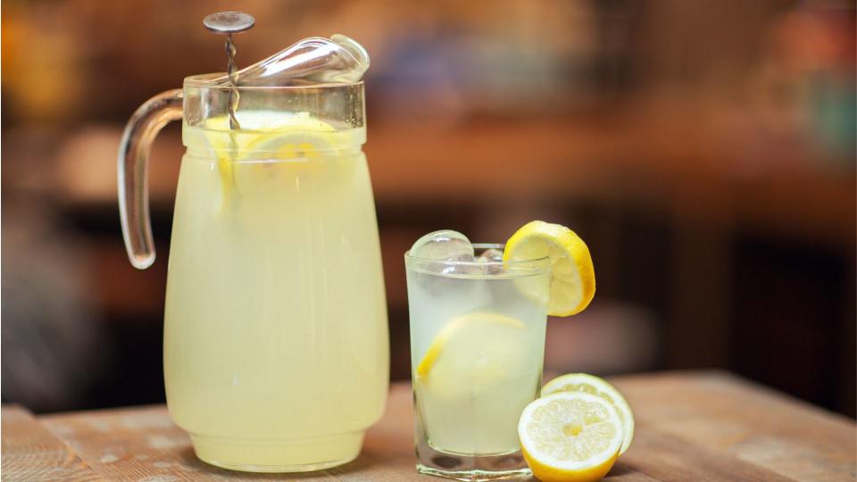 Lemonade in large glass jug and in small glass with fresh lemons on the side