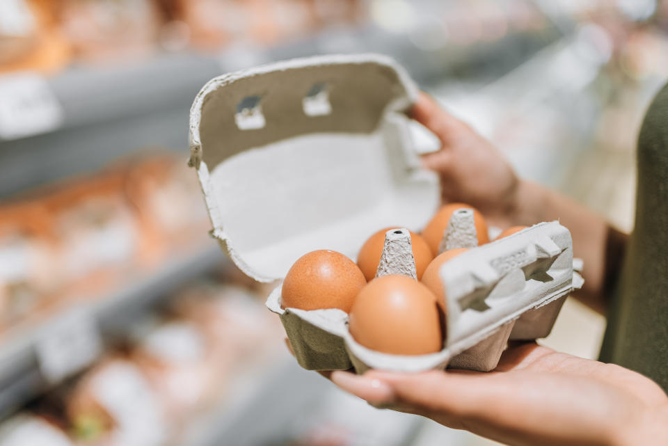 Young woman in store holding cardboard of six organic eggs.