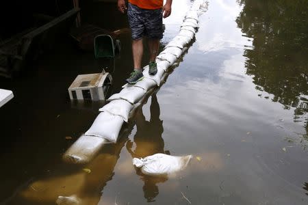 Joey Gregory's reflection is seen in flood water as he walks on top of sand bags in St. Amant, Louisiana. REUTERS/Jonathan Bachman