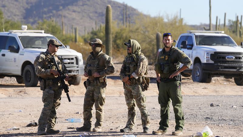 Members of the U.S. Border Patrol and U.S. Customs and Border Protection keep an eye on hundreds of migrants gathering along the border on Dec. 5, 2023, in Lukeville, Ariz. The U.S. Border Patrol says it is overwhelmed by a shift in human smuggling routes, with hundreds of migrants from faraway countries like Senegal, Bangladesh and China being dropped in the remote desert area in Arizona.