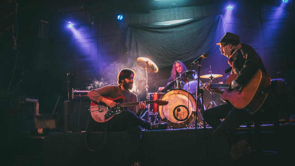 Group of people, men and woman, young band, playing music instruments indoors on stage.