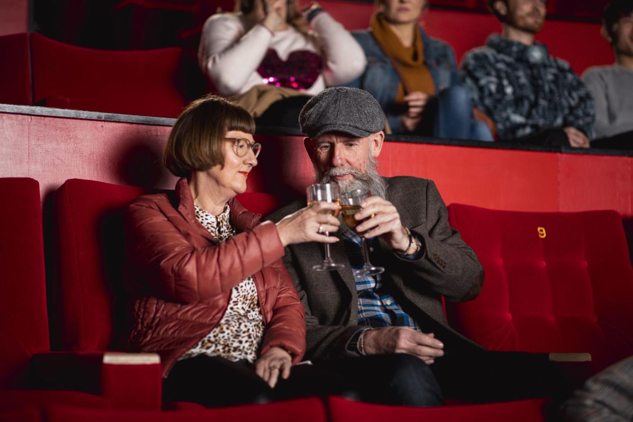 Senior couple sitting in the cinema. They are both using their smart phones before the film starts.