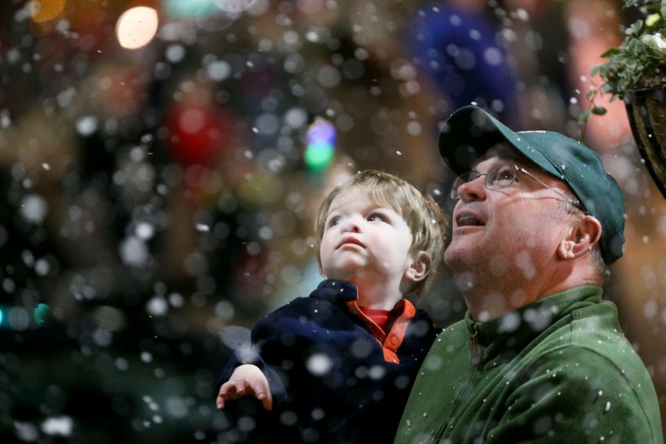 James Owens holds his son Everett as they watch artificial snow fall during Dickens Downtown along Main Ave. Tuesday, Dec. 4, 2018.  [Staff Photo/Gary Cosby Jr.]