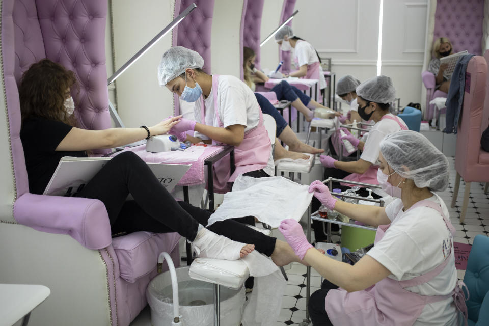 Nail technicians wearing face masks and gloves perform manicure and pedicure for their clients in a nail bar in Moscow, Russia, Tuesday, June 9, 2020. The Russian capital on Tuesday has ended a tight lockdown in place since late March, citing a slowdown in the coronavirus outbreak. Starting from Tuesday, Moscow residents are no longer required to self-isolate at home or obtain electronic passes for traveling around the city. (AP Photo/Pavel Golovkin)