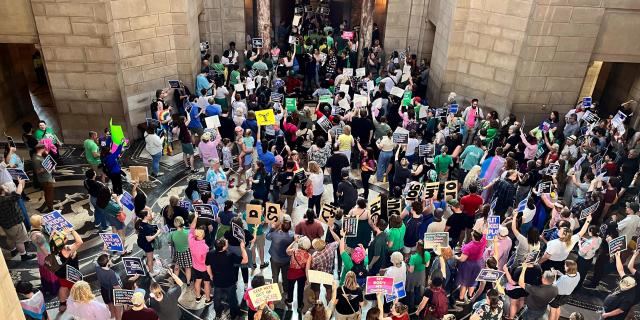 large crowd of protesters with signs gather in the nebraska state capitol rotunda