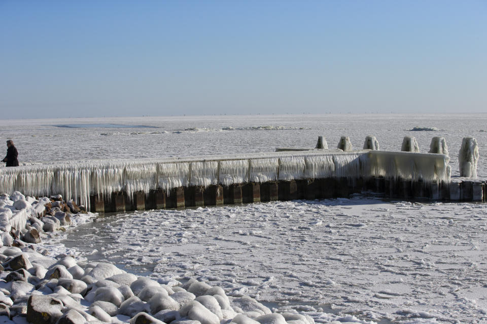 A woman takes pictures of icicles on a jetty at the Afsluitdijk, a dike separating IJsselmeer inland sea, rear, and the Wadden Sea, Netherlands, Thursday, Feb. 11, 2021. The deep freeze gripping parts of Europe served up fun and frustration with heavy snow cutting power to some 37,000 homes in central Slovakia. (AP Photo/Peter Dejong)