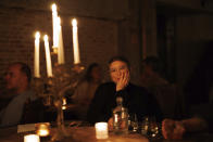 A woman waits for her dinner to arrive as she sits at a table with a candelabra at Brasserie Surrealiste in Brussels, Wednesday, Sept. 28, 2022. A group of restaurant owners in Brussels has imagined how a future without gas and electricity would look like for gourmets. Dinner guests, served at the Brasserie Surrealiste and cooked by Racines restaurant employees, were the first to experience it: No ovens, no stoves, no hot plates, no coffee machines and no light bulbs. (AP Photo/Olivier Matthys)