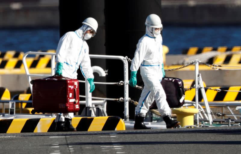 Officers in protective gears carry luggage cases after people who were transferred from cruise ship Diamond Princess, arrive at a maritime police's base in Yokohama