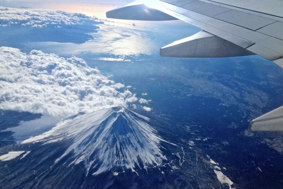 View of snow-capped Mount Fuji from airplane flying with wing in the distance of window