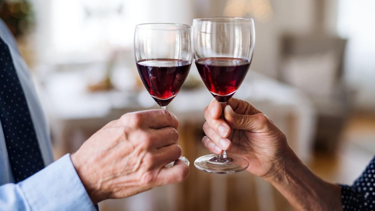 unrecognizable senior couple holding wine indoors at christmas time, clinking glasses