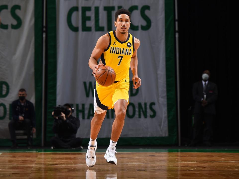 Malcolm Brogdon dribbles the ball up the floor as a Celtics championship banner hangs in the background.
