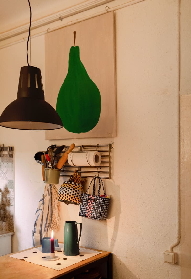 Kitchen utensils hung under green pear art in neutral room.