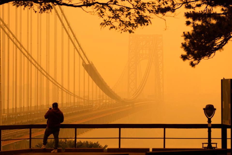 A man talks on his phone as he looks through the haze at the George Washington Bridge from  Fort Lee, N.J., Wednesday, June 7, 2023. Intense Canadian wildfires are blanketing the northeastern U.S. in a dystopian haze, turning the air acrid, the sky yellowish gray and prompting warnings for vulnerable populations to stay inside.