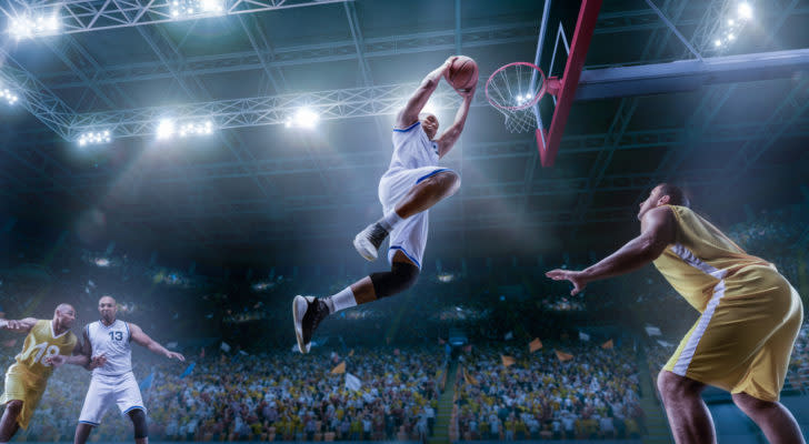 A basketball player makes a slam dunk in a crowded arena.